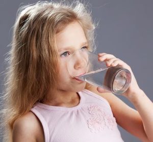 Bambina si disseta sorseggiando un bicchiere di acqua fresca