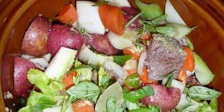 Pentola di terracotta contenente carne e verdure da cuocere