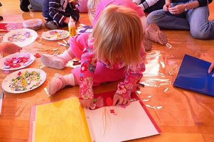Bambina disegna coi pastelli di cera su pavimento protetto dal nylon