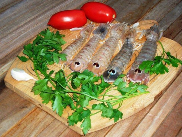 Tagliere con canocchie crude, aglio, pomodori e prezzemolo