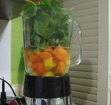 Spinaci, mango, papaya e ananas nel bicchiere del frullatore