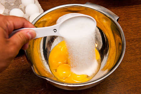 Zucchero varsato su uova sgusciate in una ciotola dalle pareti alte