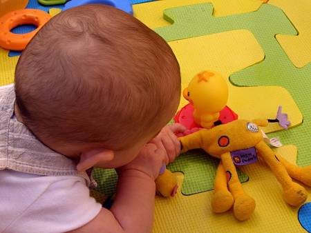 Bebè si porta alla bocca i giocattoli sul tappeto gioco