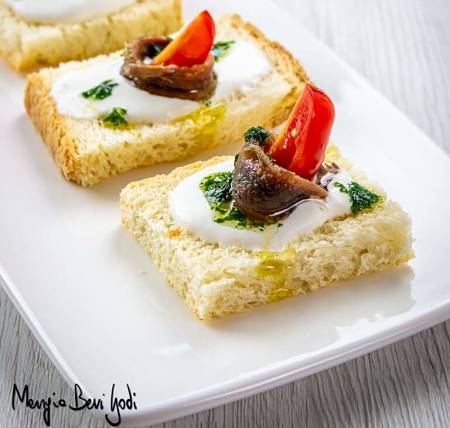 Tartine con burrata, alici decorata con pomodorino e salsa verde