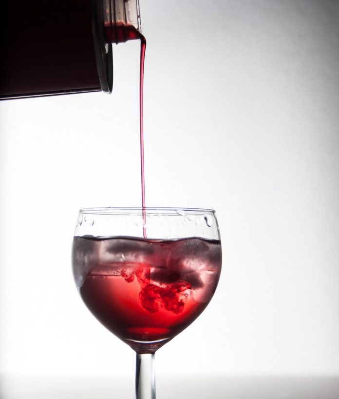 Sciroppo di amarene fatto in casa versato in bicchiere contenente acqua