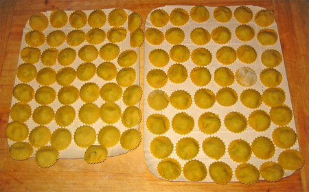 Ravioli rotondi crudi infarinati e distanziati su vassoi di cartone