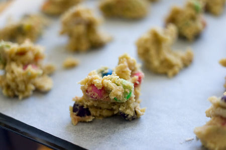 Impasto di biscotti con smarties suddiviso in mucchietti su carta da forno