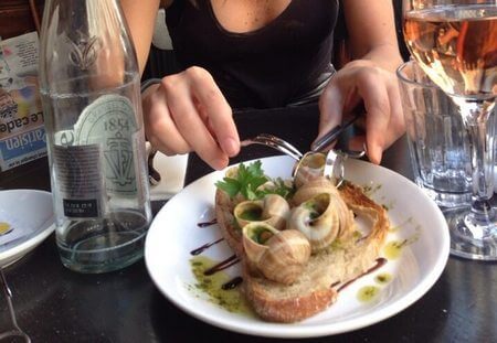 Donna mangia lumache alla bourguignonne assieme a fetta di pane abbrustolito 