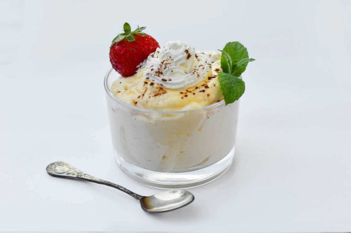 Coppetta contenente mousse di banane light senza uova e mascarpone con decorazione di panna montata, fragola fresca e cacao in polvere