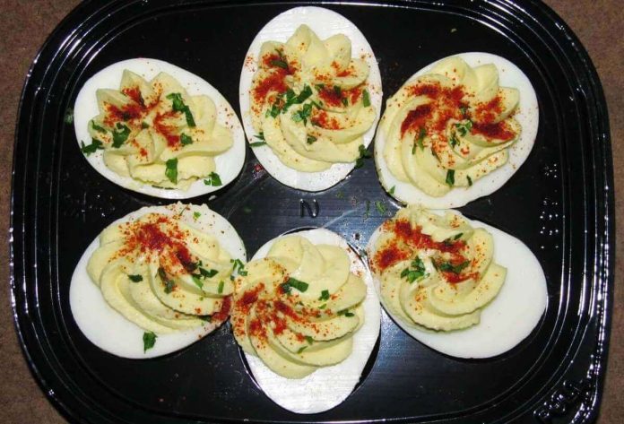 Piacevole contrasto tra i colori delle uova alla diavole e il nero del piatto di portata Uova alla diavola decorate con paprica e prezzemolo tritato su piatto di portata nero