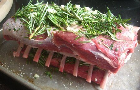 Carré di agnello crudo insaporito con erbe aromatiche, aglio, pepe e sale