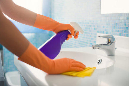 Donna pulisce il rubinetto del lavabo con detergente multiuso ecologico e spugna