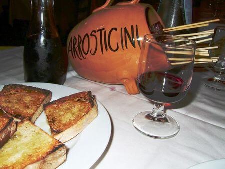 Arrosticini serviti in tavola nell'apposito contenitore di terracottacon pane abbrustolito unto di olio e vino rosso
