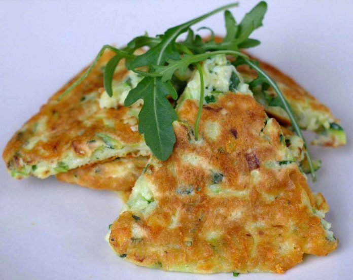 L'appetitosa frittata di zucchine senza uove vegana si può decorare con foglie di rucola Frittata di zucchine senza uova vegana tagliata a fette e decorata con foglie di rucola