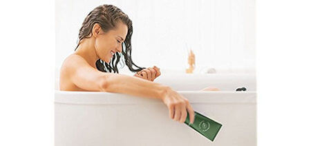Giovane donna nella vasca da bagno con balsamo applicato su capelli bagnati