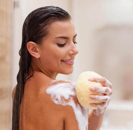 Giovane donna si lava con spugna morbida insaponata