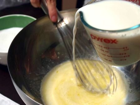 Composto di uova, burro fuso e latte mescolato con la frusta da cucina nella ciotola