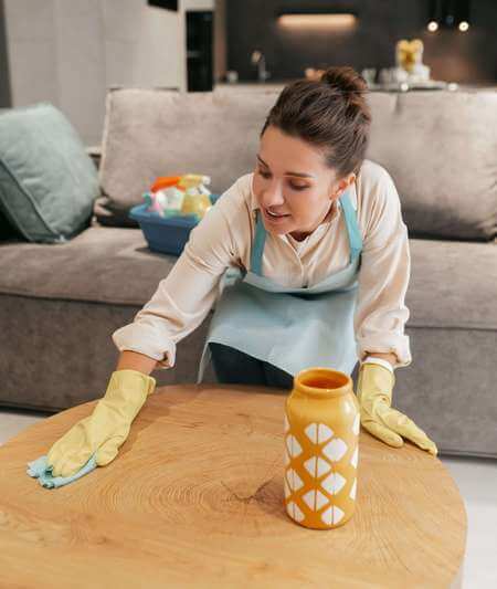 Donna nutre e ravviva il legno grezzo del tavolo passandoci sopra la crema con un panno