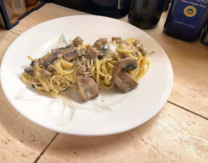 Pasta alla boscaiola con salsiccia e funghi in un piatto bianco