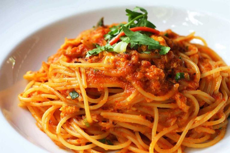 Spaghetti al granchio blu con pomodorini in piatto di ceramica bianca.
