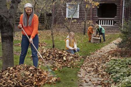 Mamma raccoglie le foglie morte in giardino con l'aiuto dei suoi bambini