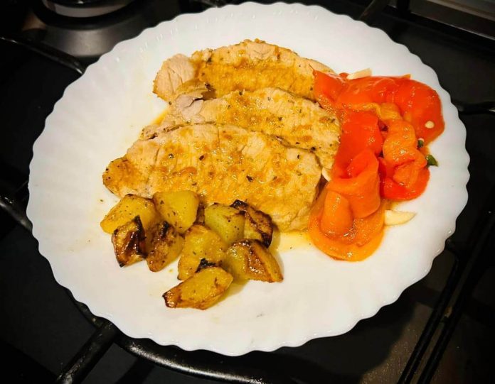 Piatto con dentro arista all'arancia al forno affettata, patate arrostite e peperoni grigliati