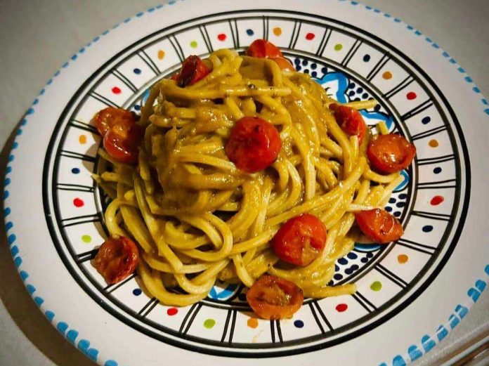 Spaghetti conditi con crema di melanzane, pomodorini e alici impiattati