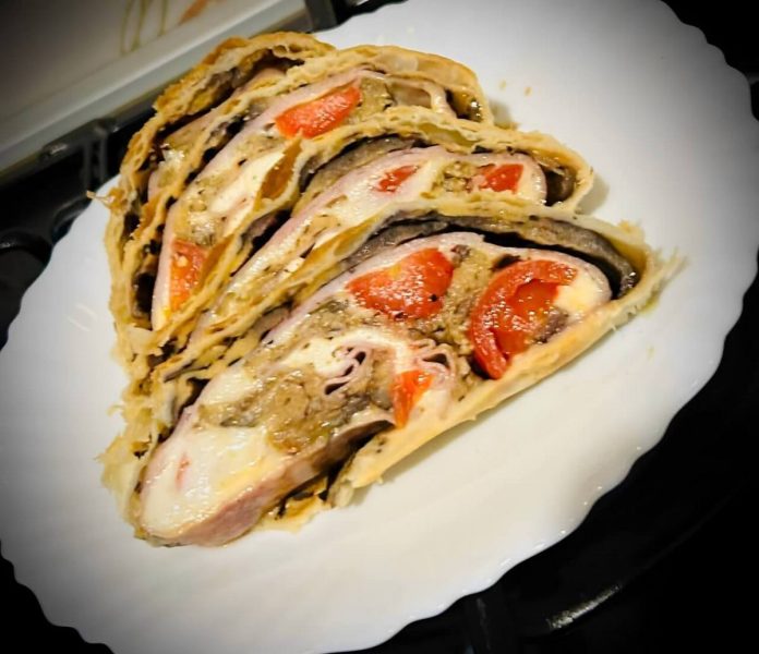 Fette di rotolo di pasta sfoglia ripieno di melanzane, prosciutto, scamorza e pomodorini