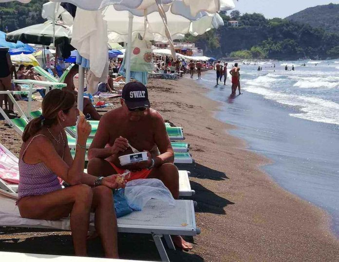 UOmo e donna consumano cibi portati da casa sotto l'ombrellone del lido Coppia di bagnanti mangia i propri cibi in spiaggia