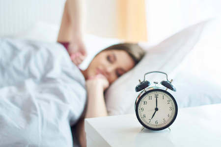 Donna dormiente con sveglia sul comodino