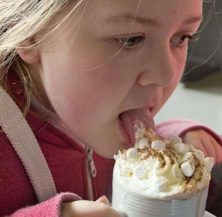 Bimba intenta a leccare la panna di decorazione della cioccolata calda