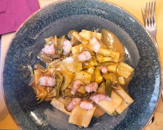 Paccheri con carciofi e gamberi crudi su piatto di ceramica scuro