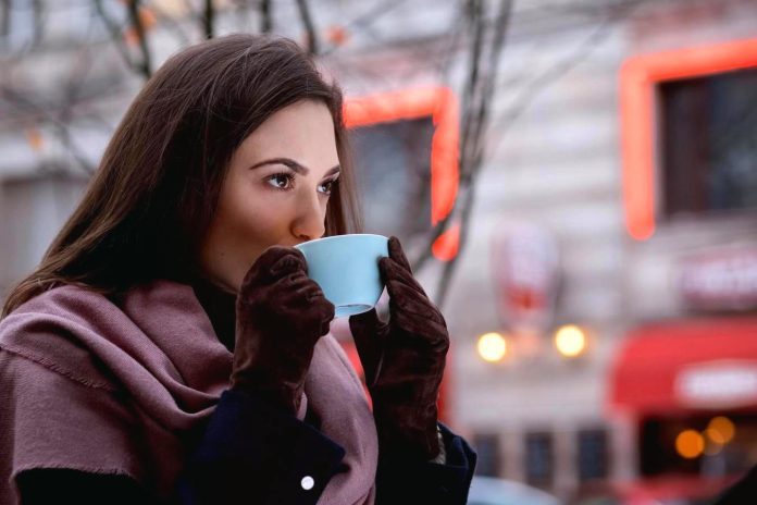 Donna attraente beve il caffè all'aperto in una mattina invernale Donna gusta il caffè a metà mattina all'aperto in inverno