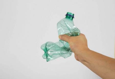 Mano maschile schiaccia una bottiglia di plastica erroneamente 
