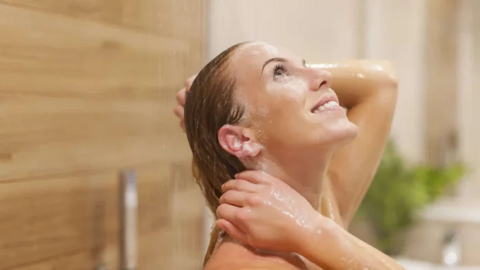 Donna sorride e si rinfresca sotto la doccia Donna sorridente fa una doccia rinfrescante in estate