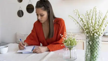 Ragazza scrive il diario con vasi di fiori accanto 