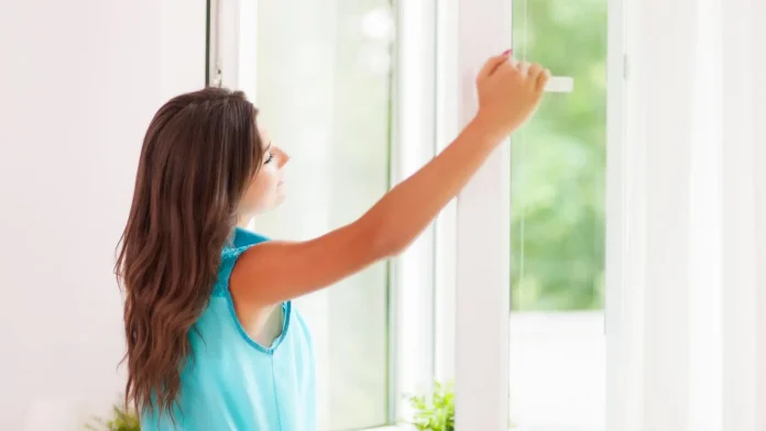 Giovane donna apre la finestra per arieggiare la casa